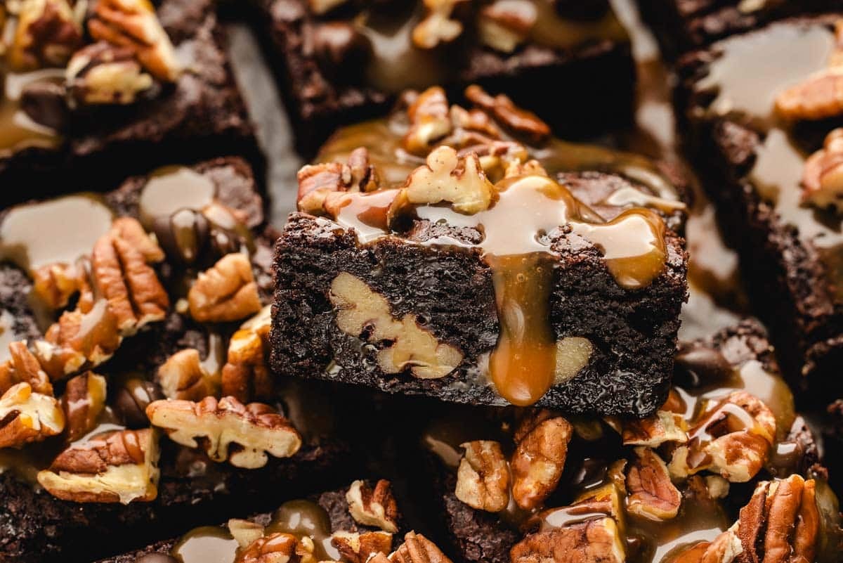 Close-up of turtle chocolate brownies topped with pecans and drizzled with caramel sauce.