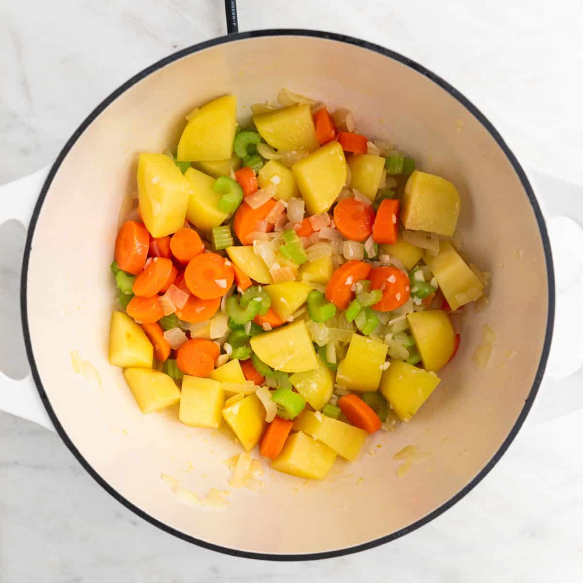 Vegetables sautéed in olive oil in a large pot.