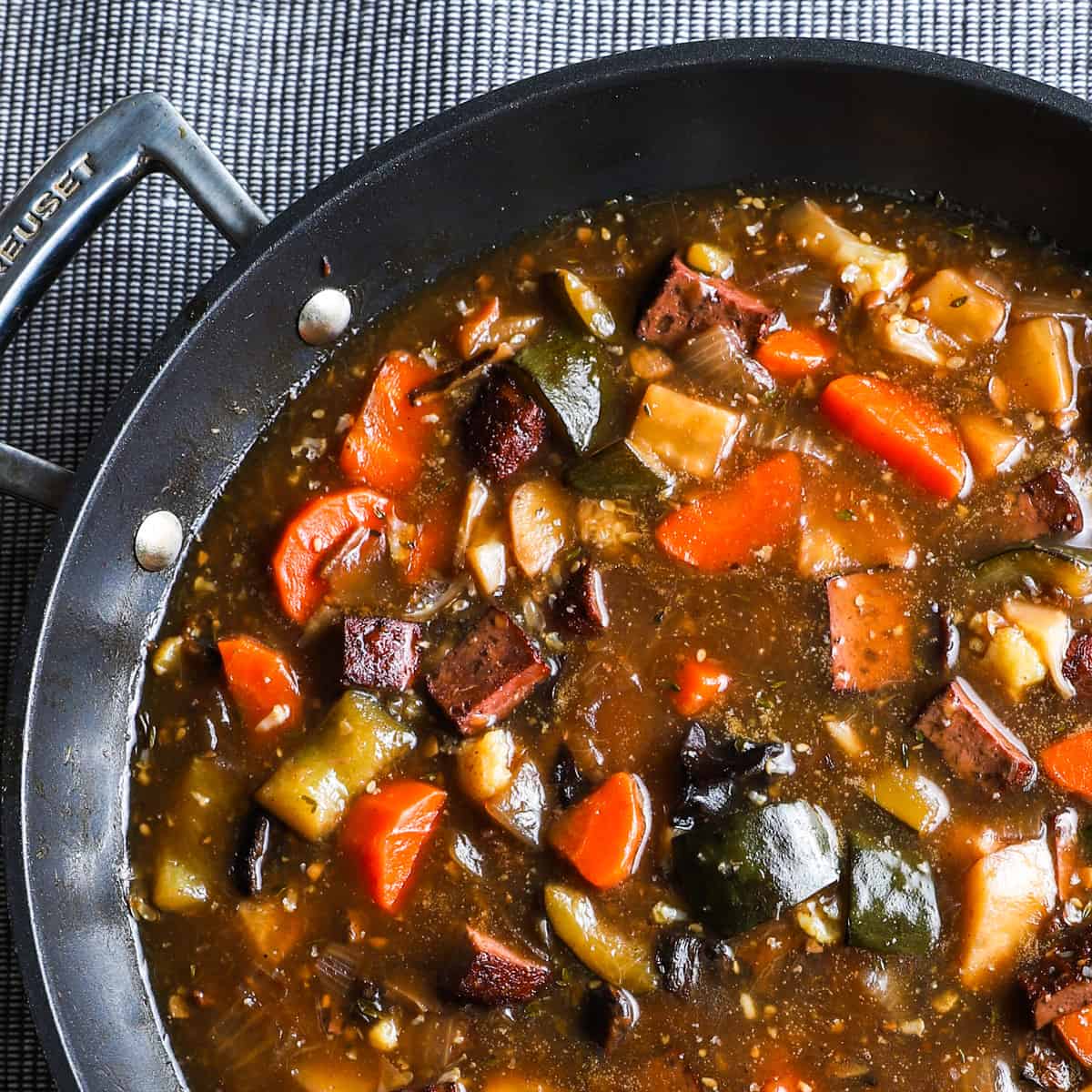 1x1 photo of vegan stew in a black large saute pan on a grey textured table cloth.