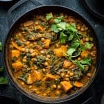 Plant based chickpea, sweet potato and spinach curry in a black cast iron pan on a black background.