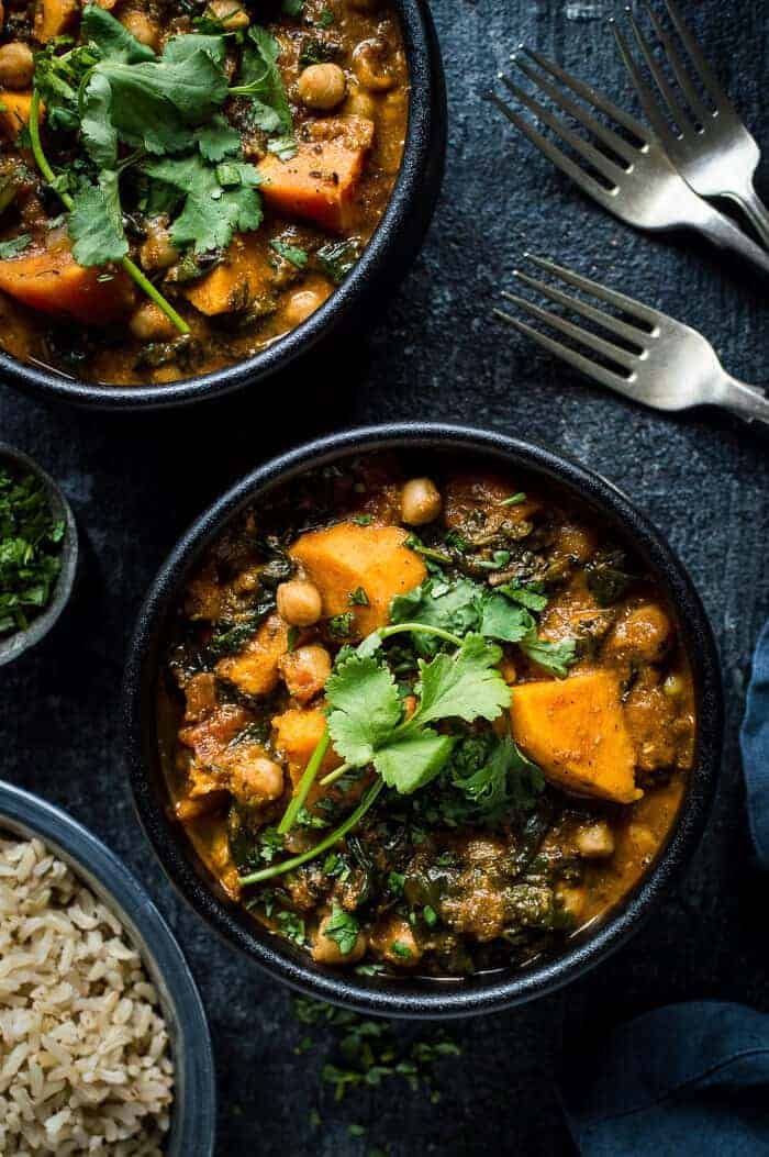 Two black bowls of vegan chickpea, sweet potato and spinach curry on a black background.