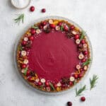 Vegan cranberry curd tart on a white plate on a white surface with a bowl of pearl sugar.