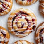Close up of vegan cranberry orange rolls on a white surface.