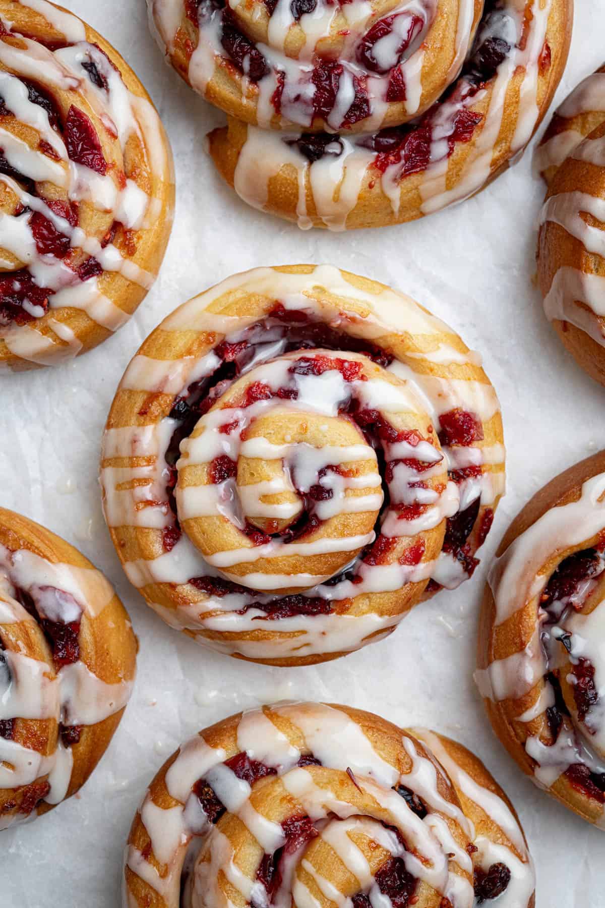Close up of vegan cranberry orange rolls on a white surface.