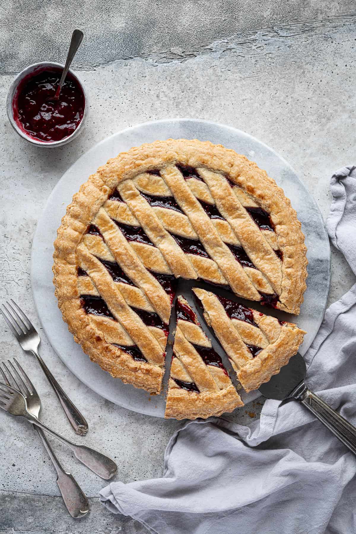Vegan jam crostata on a marble board with forks and a bowl of jam.