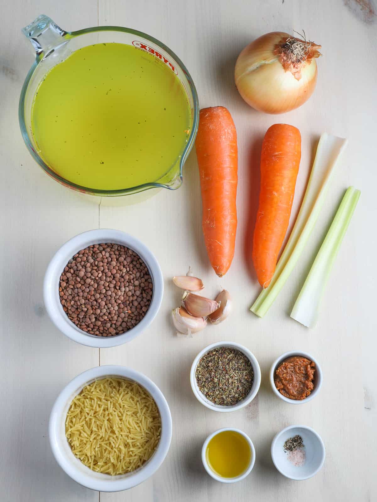 Photo showing the ingredients for this vegan lentil & vegetable noodle soup all laid out individually on a whitewashed table.