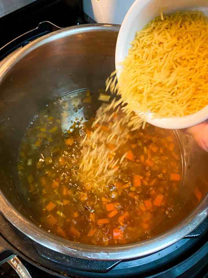 Photo showing cooked soup with noodles being added from a bowl.
