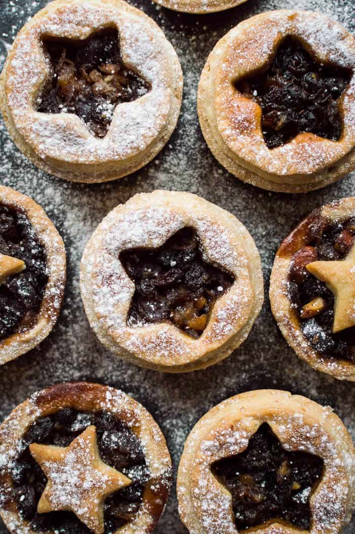 a close up of vegan mince pies with coconut oil pastry dusted with icing sugar on a black background.