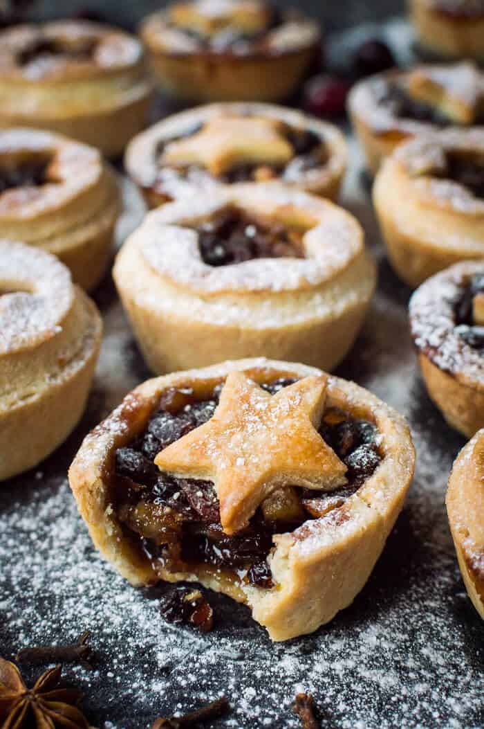 Close up of an icing sugar dusted vegan mince pie with a bite taken out.