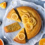 Vegan semolina cake cut into slices on a sheet of baking parchment on a grey background with sliced oranges and lemons