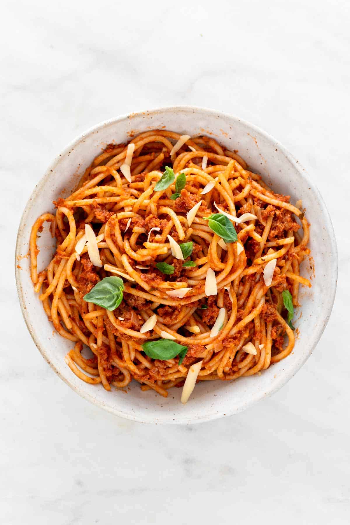 Vegan spaghetti in a bowl garnished with basil and vegan cheese.