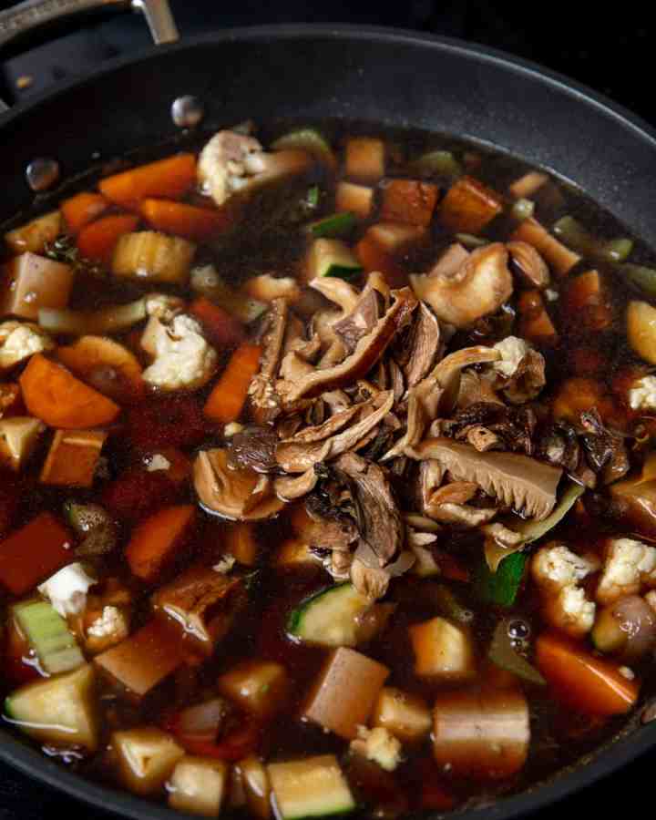 Photo of soaked mushrooms and mushroom soaking water being stirred in to the pan.