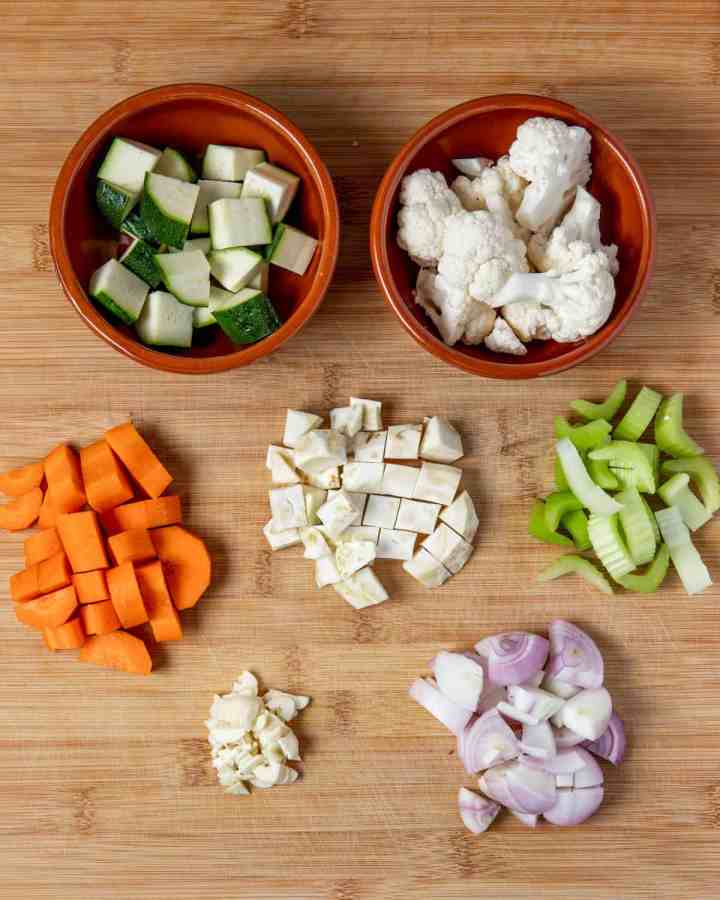 Photo showing each of the vegetables cut into chunks in little piles on a wooden chopping board.
