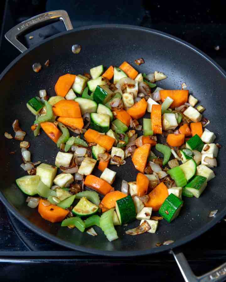 Photo of frying onions, carrot, celery and courgette in a pan.